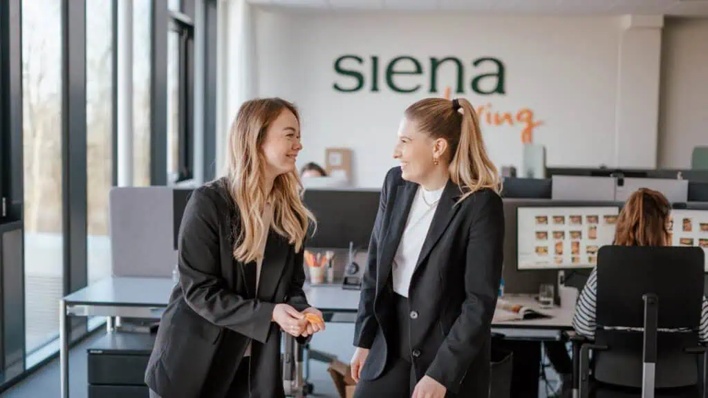 Zwei junge Frauen lachen gemeinsam in einem modernen Büro von SIENA GARDEN.